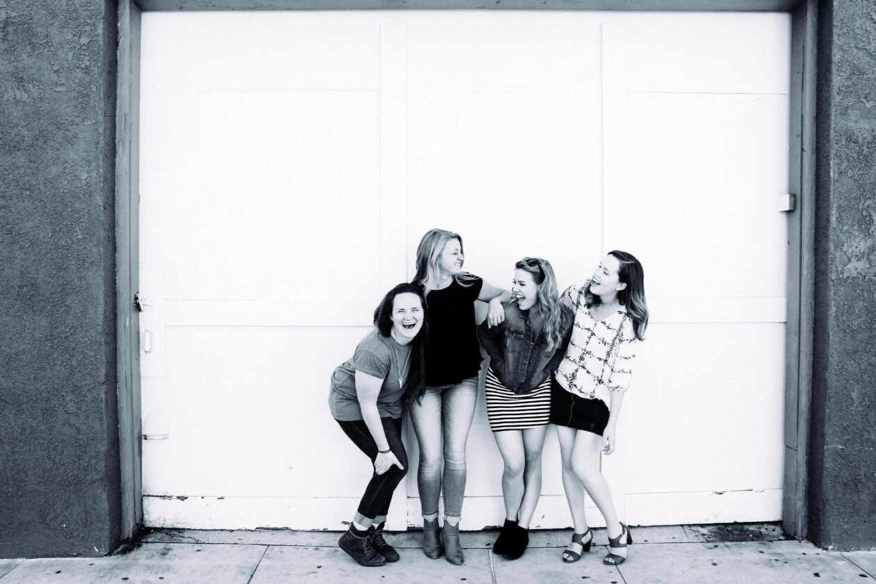 Four young women laughing together in front of an urban door, showcasing friendship and happiness.
